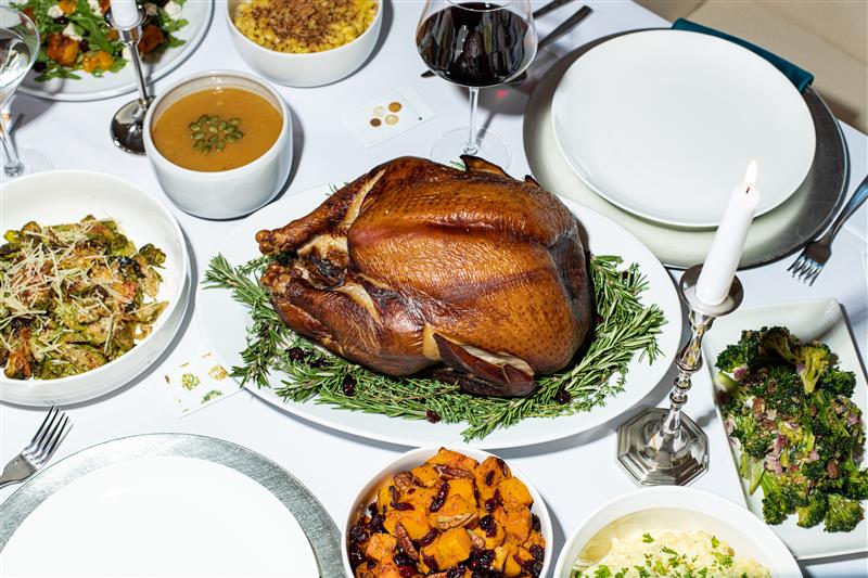 Table with a turkey, plates, wine and food on it for Thanksgiving